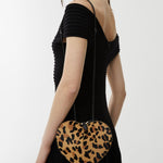 Woman holding a heart-shaped clutch with leopard print design on a white background