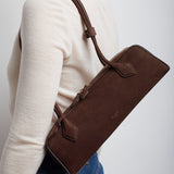 Person wearing a brown leather crossbody bag on a plain background