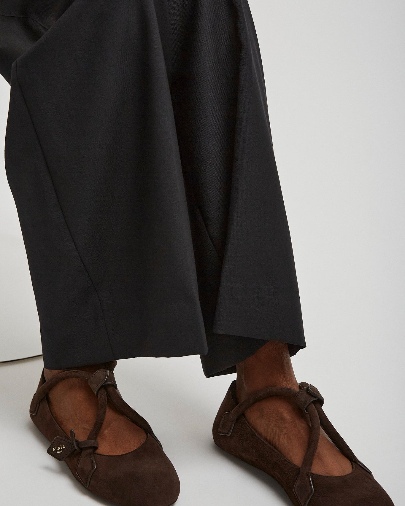 Brown ballet flats worn with black pants on a white background