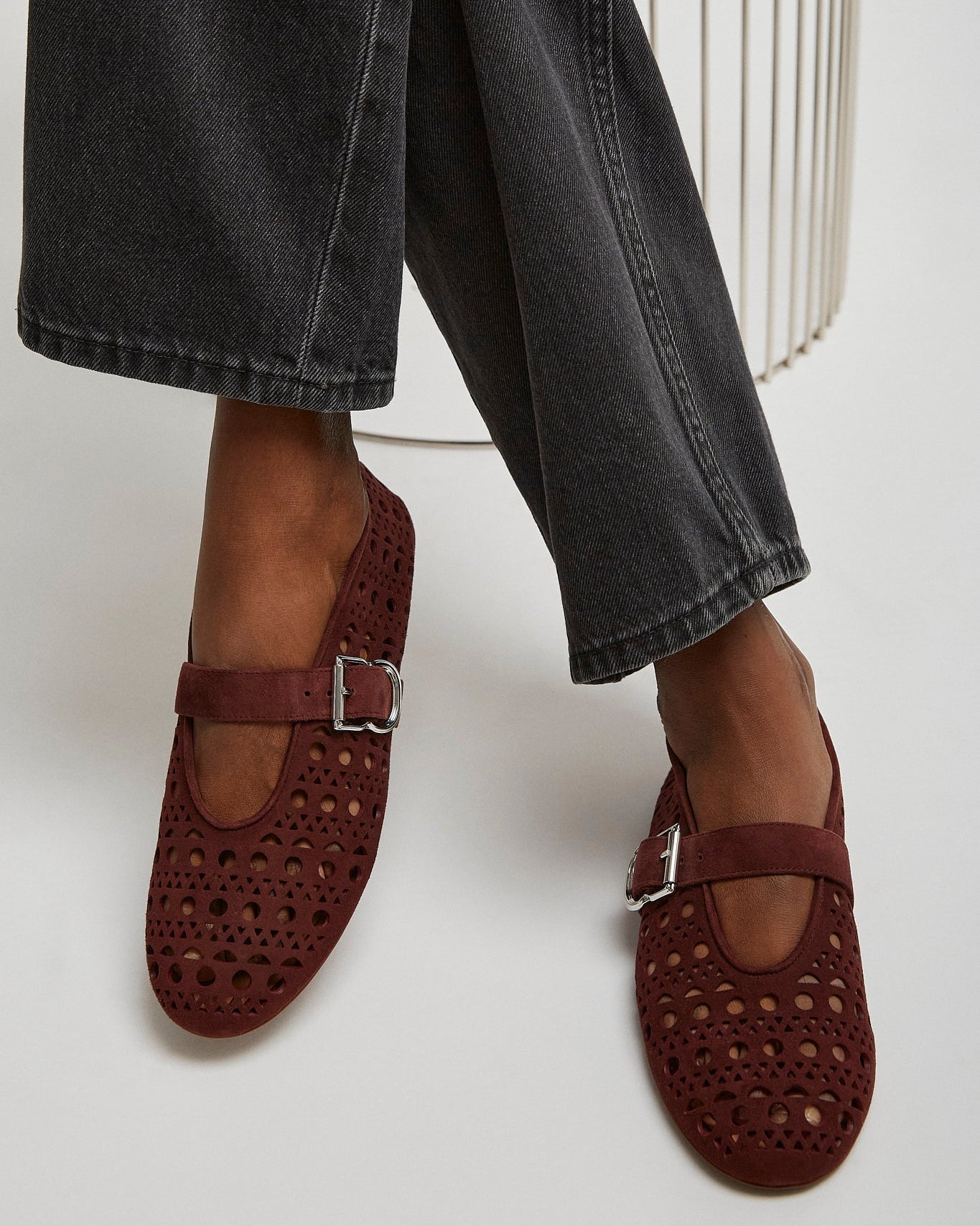 Brown perforated loafers worn with black jeans on a white background