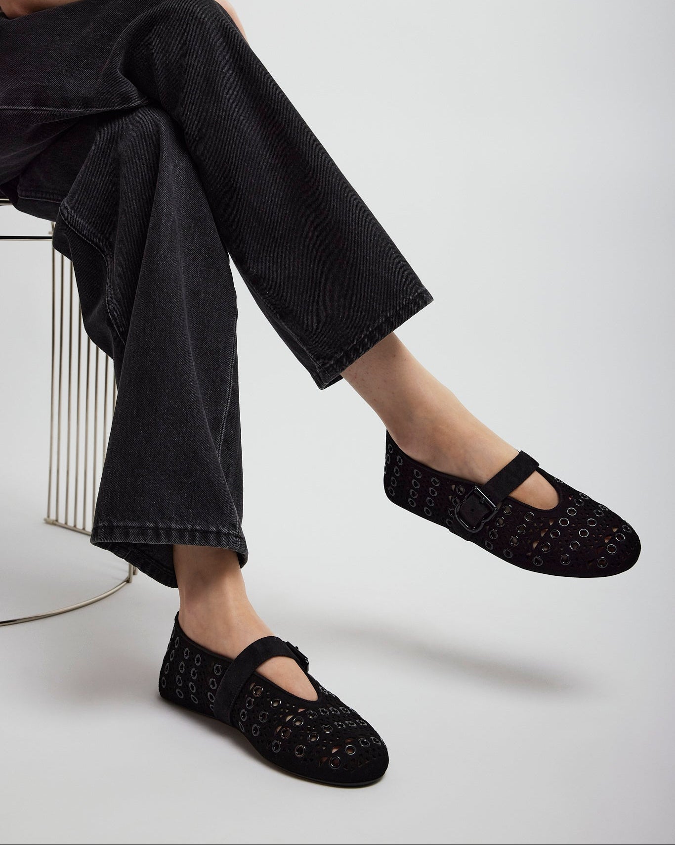 Person wearing black flats and black pants sitting on a white background