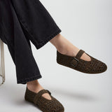 Brown perforated shoes worn with black pants on a light gray background