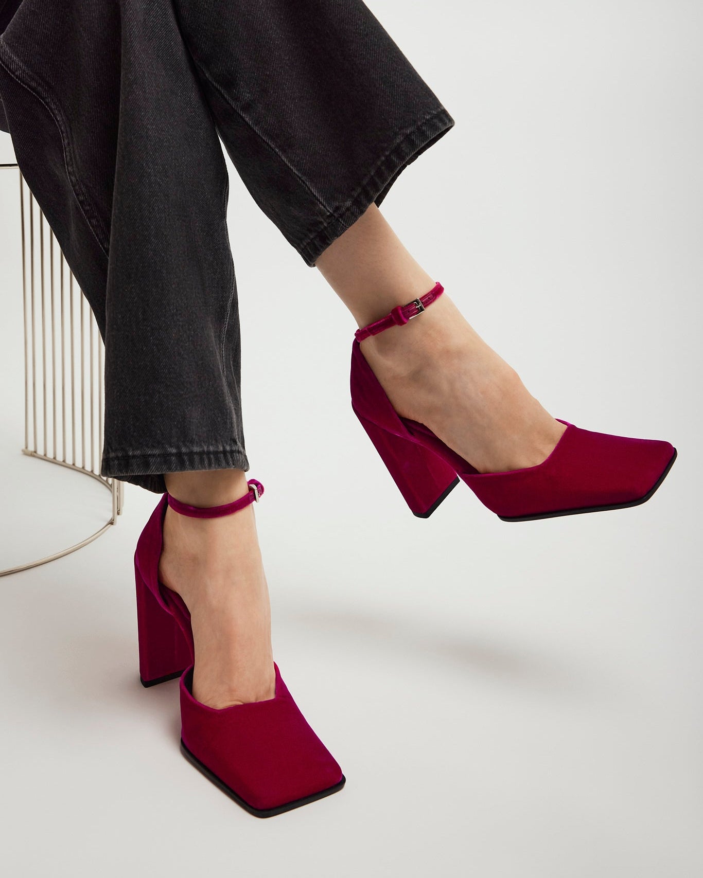 Red high-heeled shoes worn with black pants on a white background