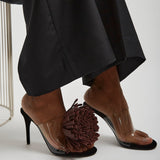 Brown high-heeled shoes with clear soles and pom-pom details worn with a black outfit.