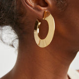 Gold hoop earring worn by a person with a neutral background