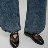 Black shoes with mesh design worn with blue jeans on a light gray background