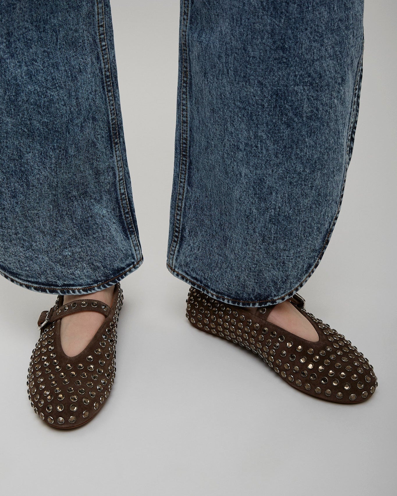 Brown studded flats worn with blue jeans on a plain background