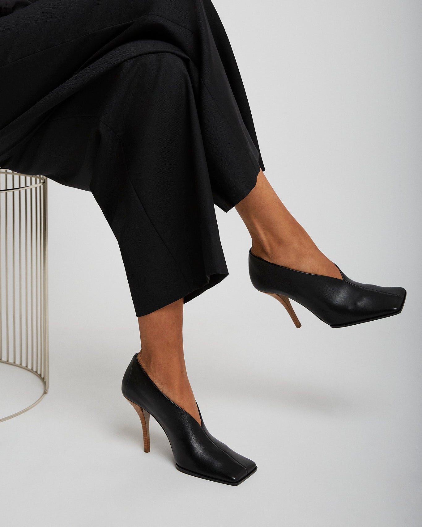 Person wearing black high-heeled shoes and black pants on a white background