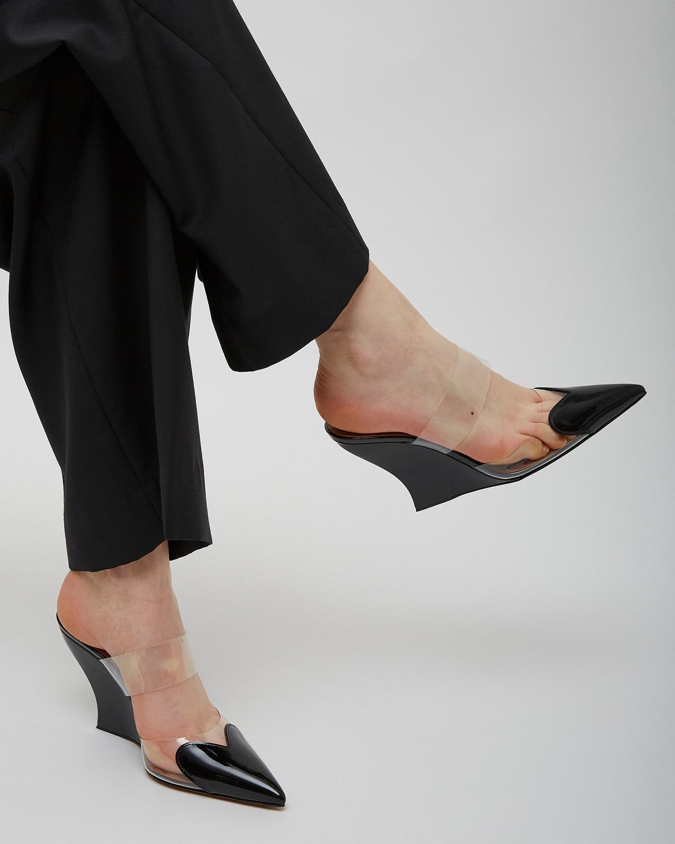 Black high-heeled shoes worn with black pants on a light gray background