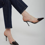 Black high-heeled shoes worn with blue jeans on a light gray background