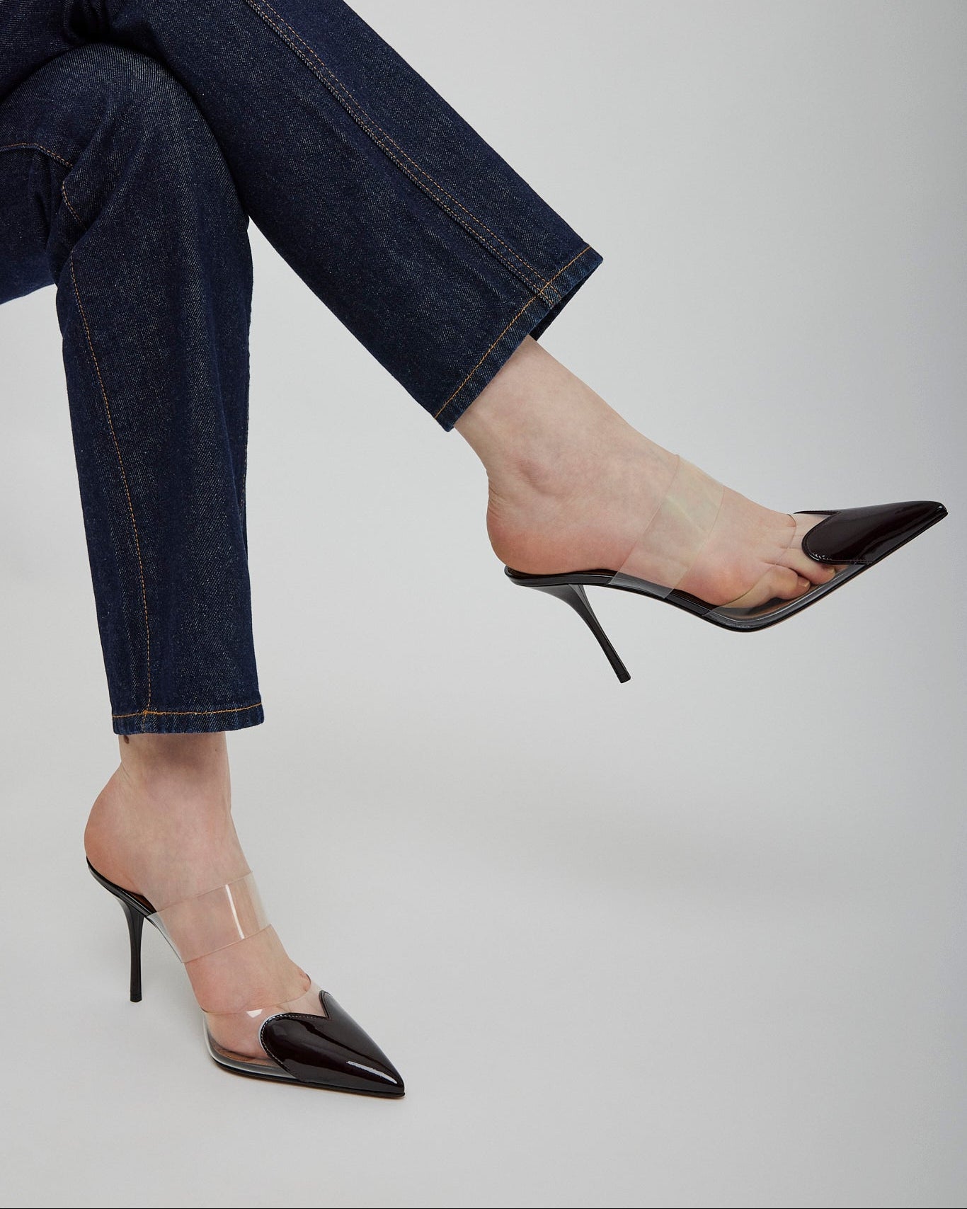 Black high-heeled shoes worn with blue jeans on a light gray background