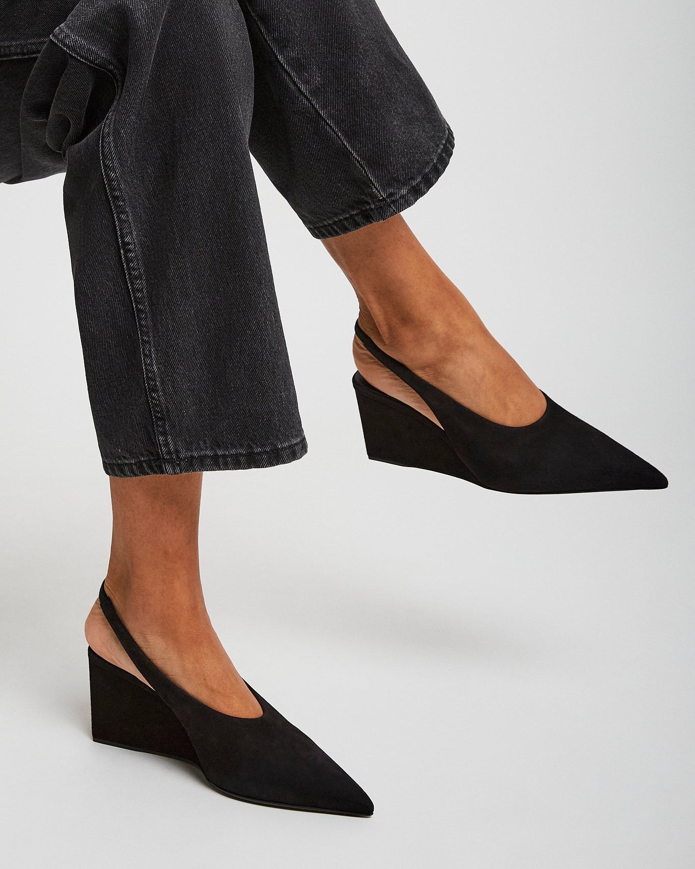 Person wearing black wedge shoes and black jeans on a light gray background