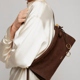 Person wearing a white satin outfit with a brown leather handbag on a neutral background