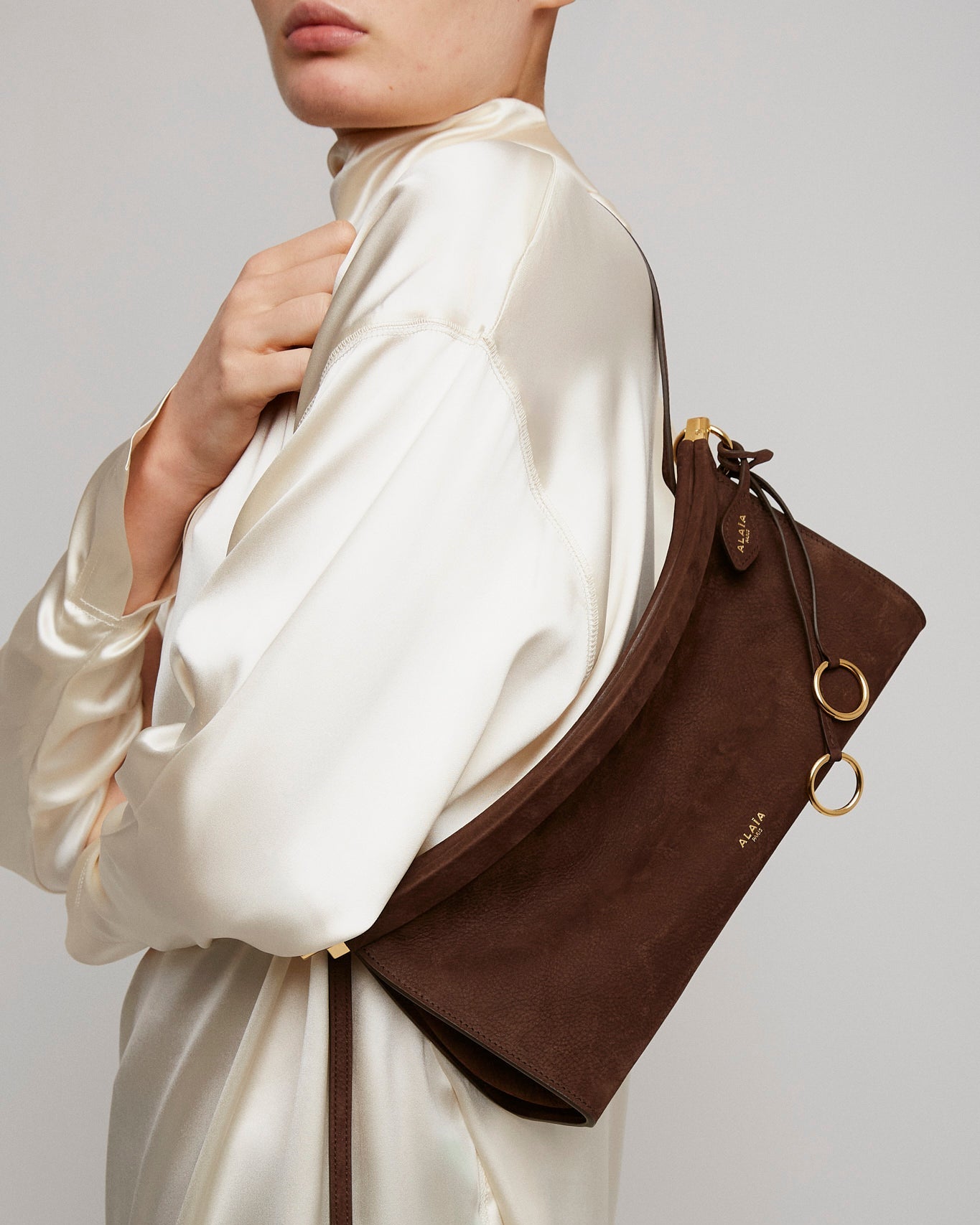 Person wearing a white satin outfit with a brown leather handbag on a neutral background