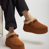 Brown platform shoes with fur trim worn by a person sitting on a chair.