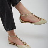 Beige flats with gold embellishments worn by a person in black pants on a white background