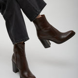 Brown leather ankle boots worn with dark jeans on a light gray background