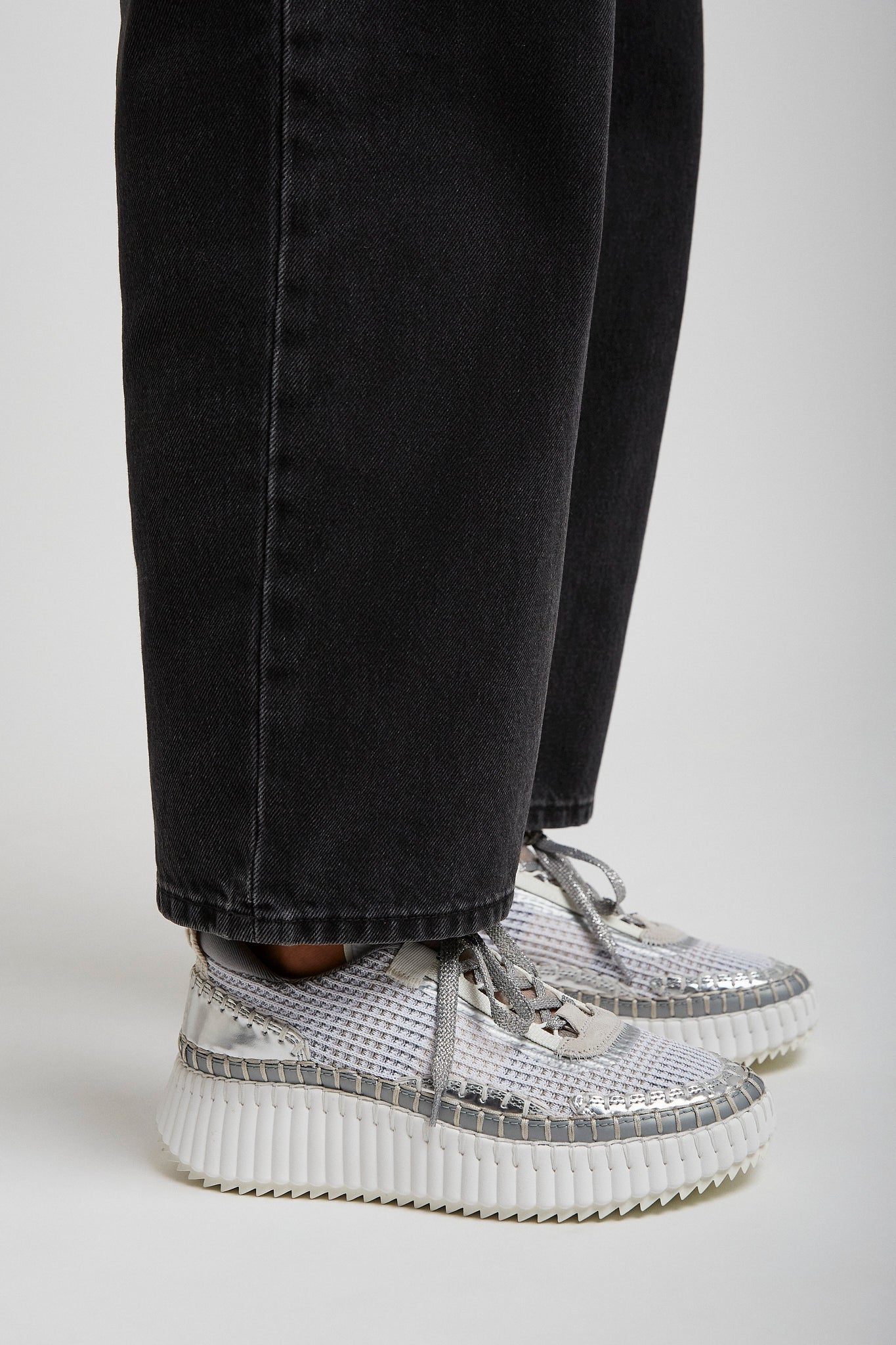 Silver high-top sneakers worn with black jeans on a light gray background