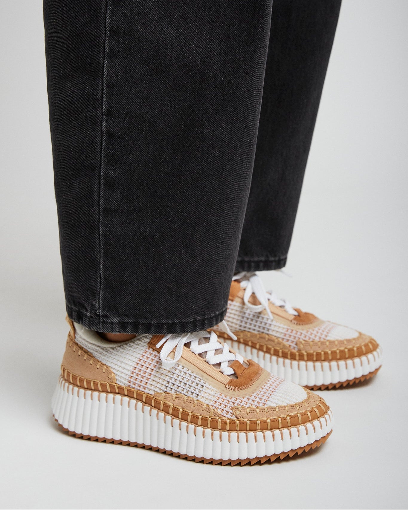 Person wearing black jeans and white sneakers with brown soles on a light gray background