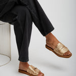 Person wearing gold sandals and black pants on a white background