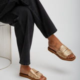 Person wearing gold sandals and black pants on a white background
