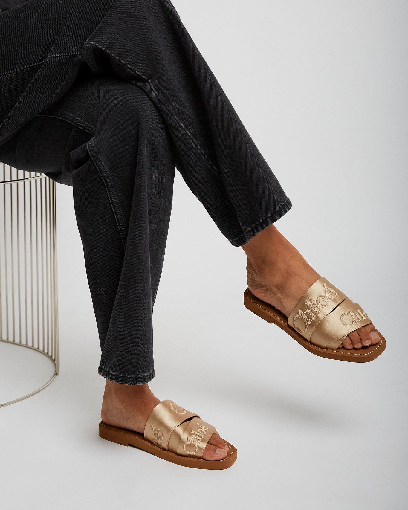 Person wearing gold sandals and black pants on a white background