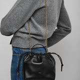 Person wearing a gray sweater with a black handbag featuring a gold chain strap on a plain background