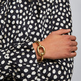 Person wearing a black and white polka dot dress with a gold bracelet on a plain background