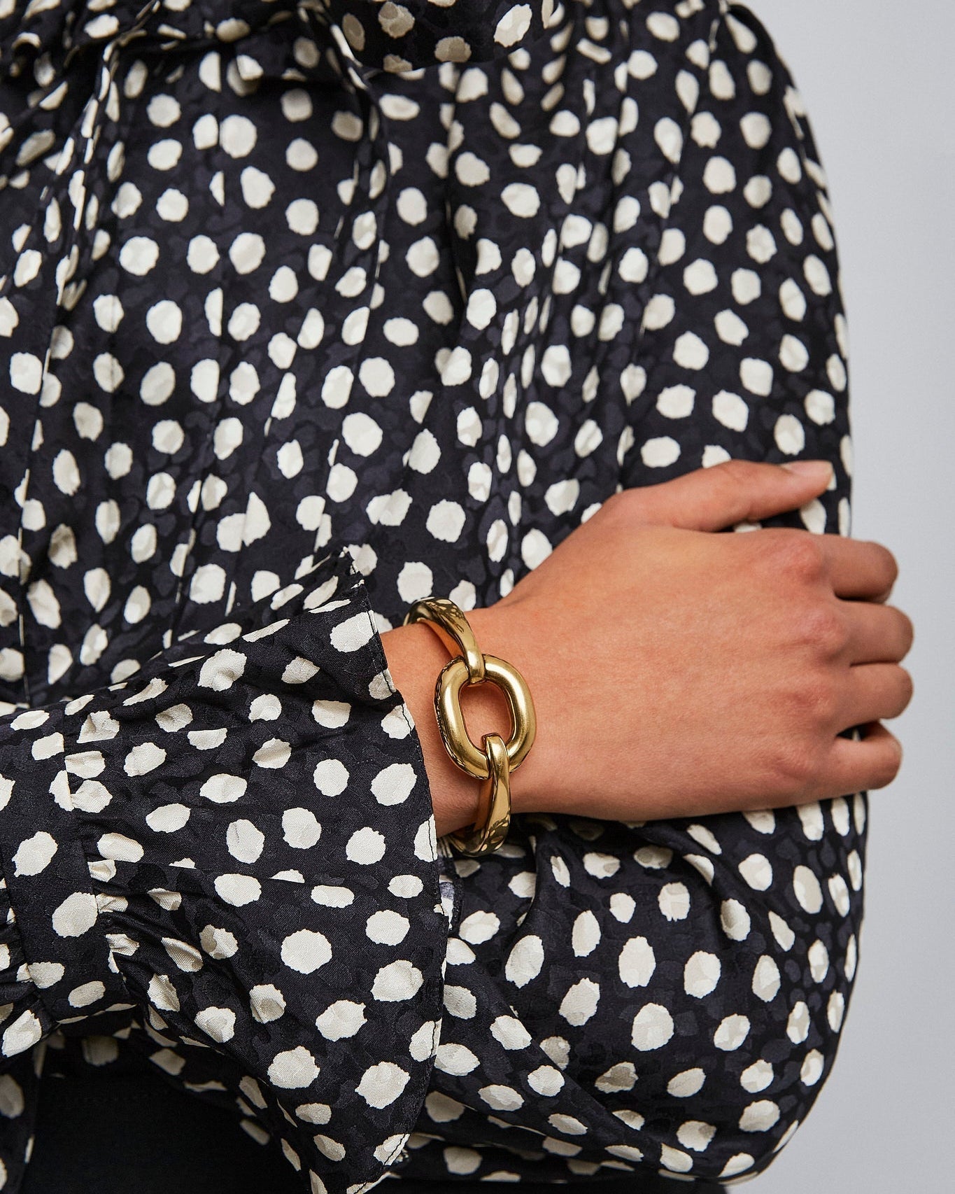 Person wearing a black and white polka dot dress with a gold bracelet on a plain background