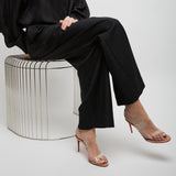 Person wearing a black outfit sitting on a wire stool against a white background
