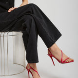 Person wearing black outfit with red high-heeled shoes sitting on a wire stool against a white background