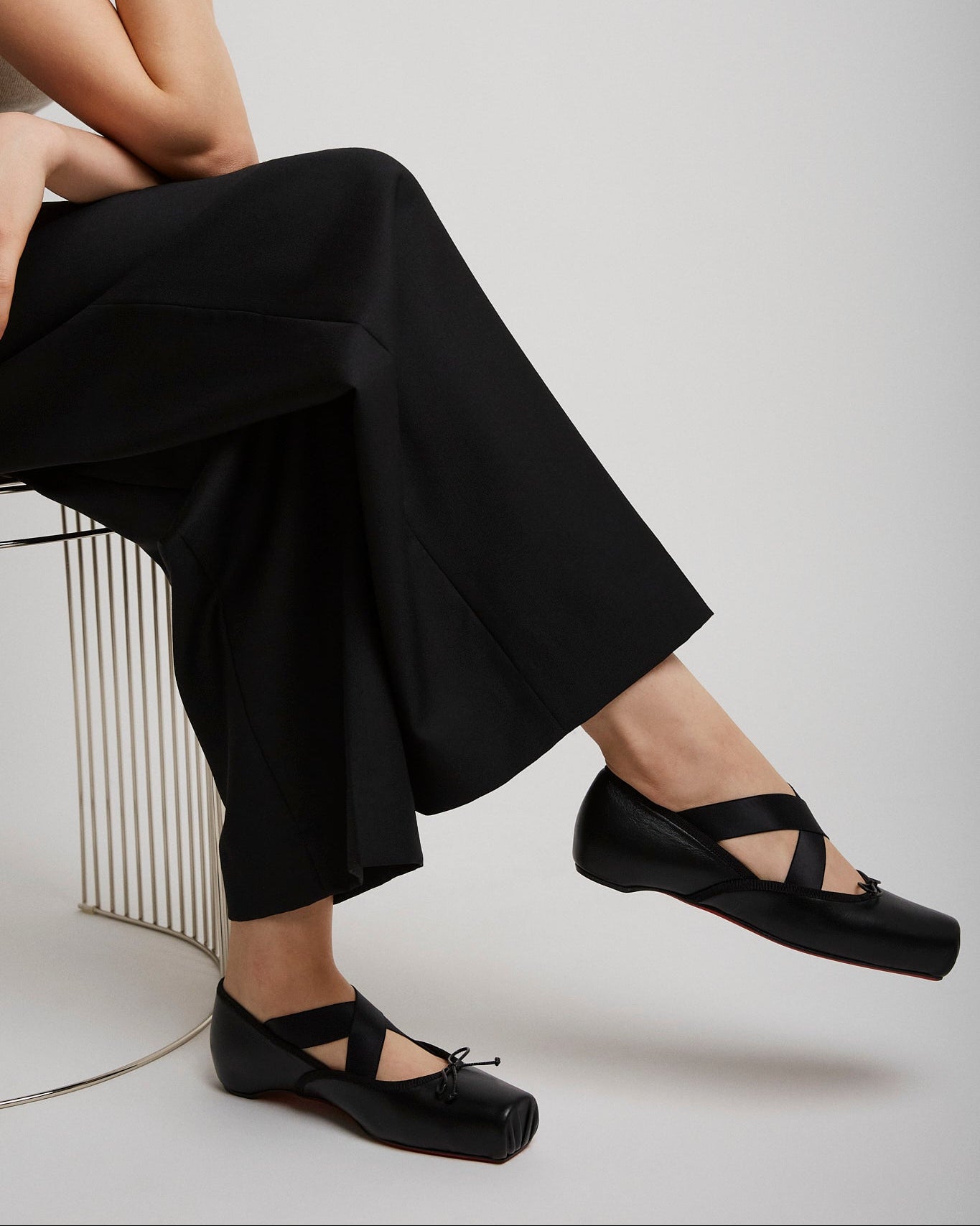 Person wearing black sandals and wide-leg pants sitting on a white background