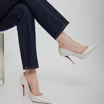 Person wearing dark jeans and white high-heeled shoes with red soles on a light gray background