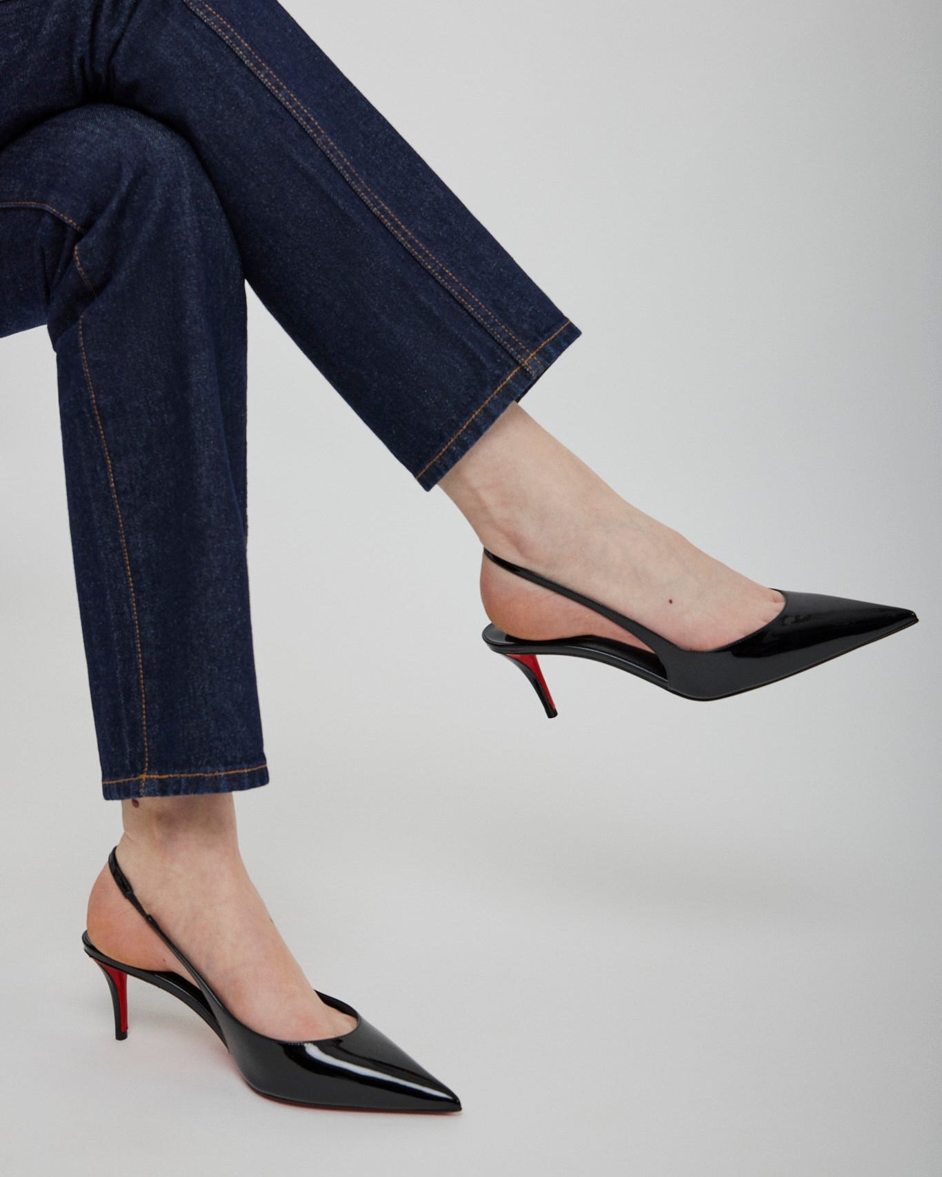 Black high-heeled shoes worn with blue jeans on a light gray background