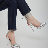 Silver high-heeled shoes worn with dark blue jeans on a light gray background