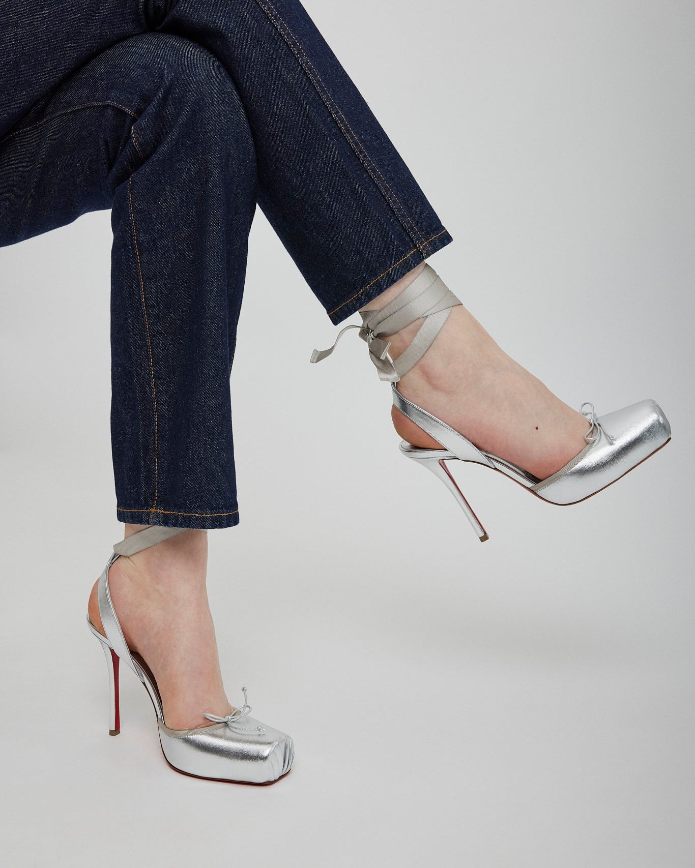 Silver high-heeled shoes worn with dark blue jeans on a light gray background