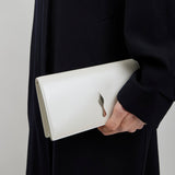 Person holding a white clutch with a subtle design against a neutral background