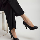 Person wearing black high-heeled shoes and pants on a white background