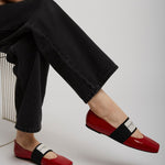 Person wearing red flats with black straps on a light gray background