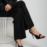 Person wearing a black outfit with high-heeled shoes sitting on a white stool against a light gray background