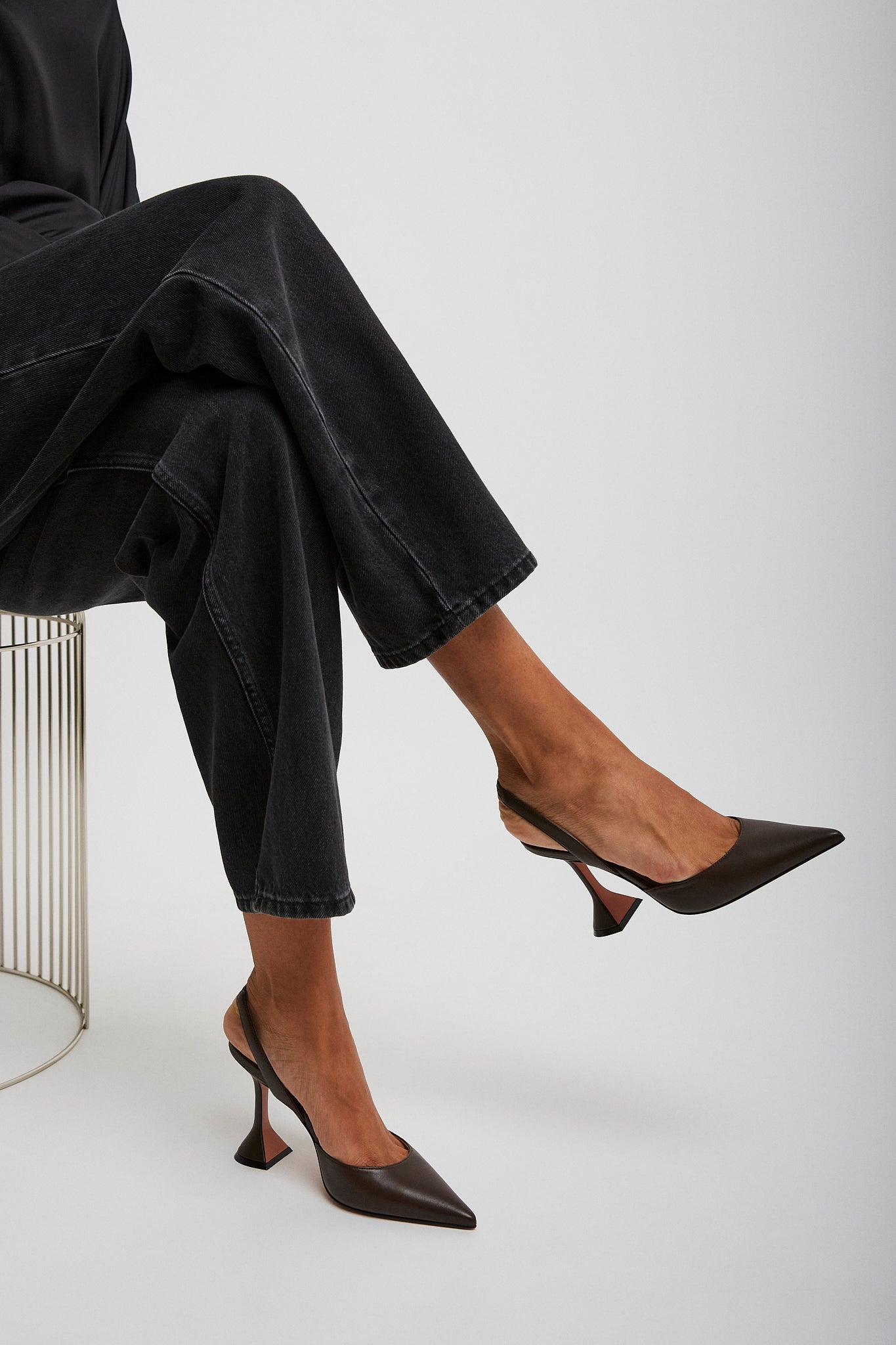 Person wearing black high-heeled shoes and dark pants sitting on a white background