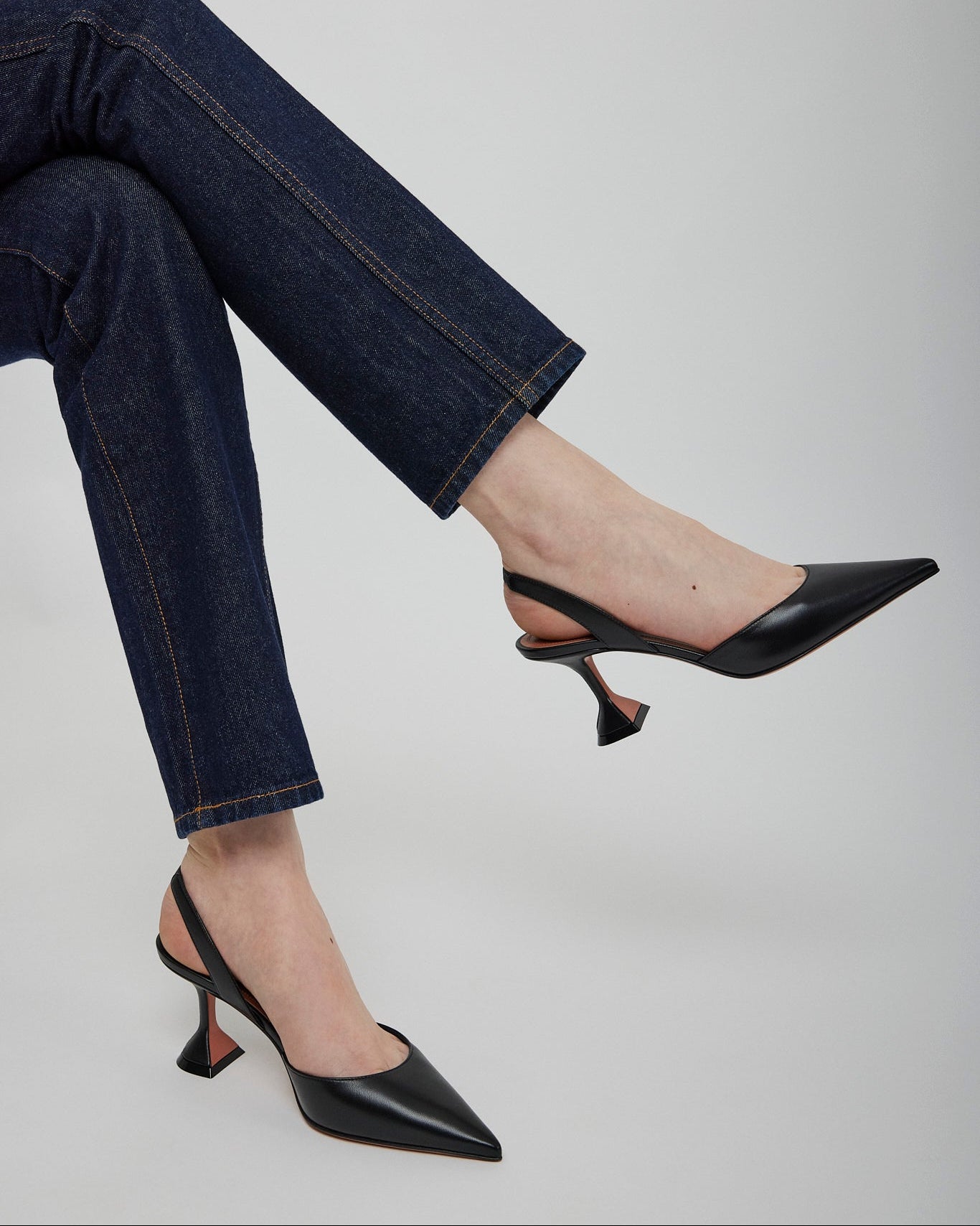 Person wearing black high-heeled shoes and blue jeans on a plain background