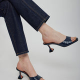 Person wearing dark blue high-heeled shoes and jeans on a plain background