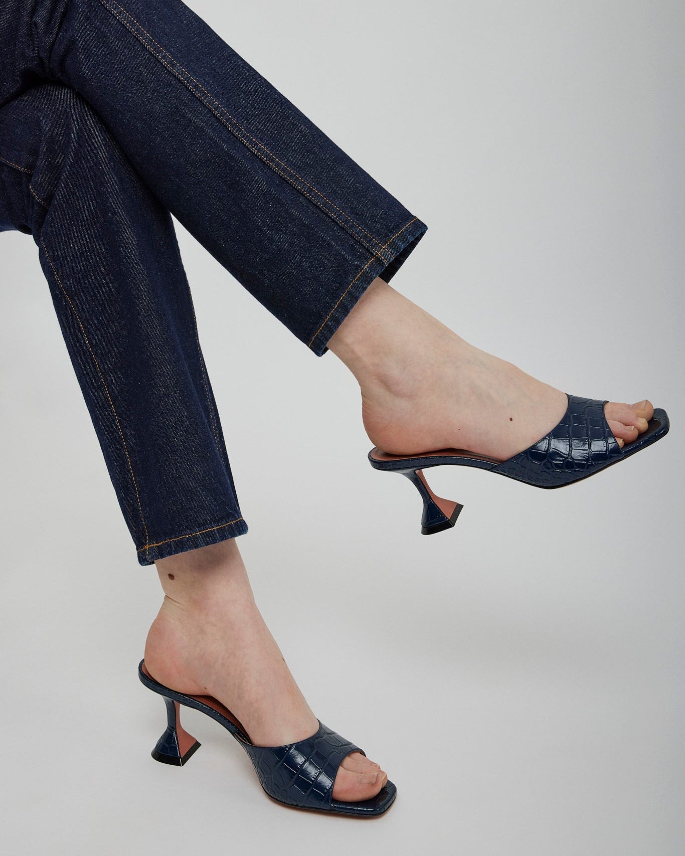 Person wearing dark blue high-heeled shoes and jeans on a plain background