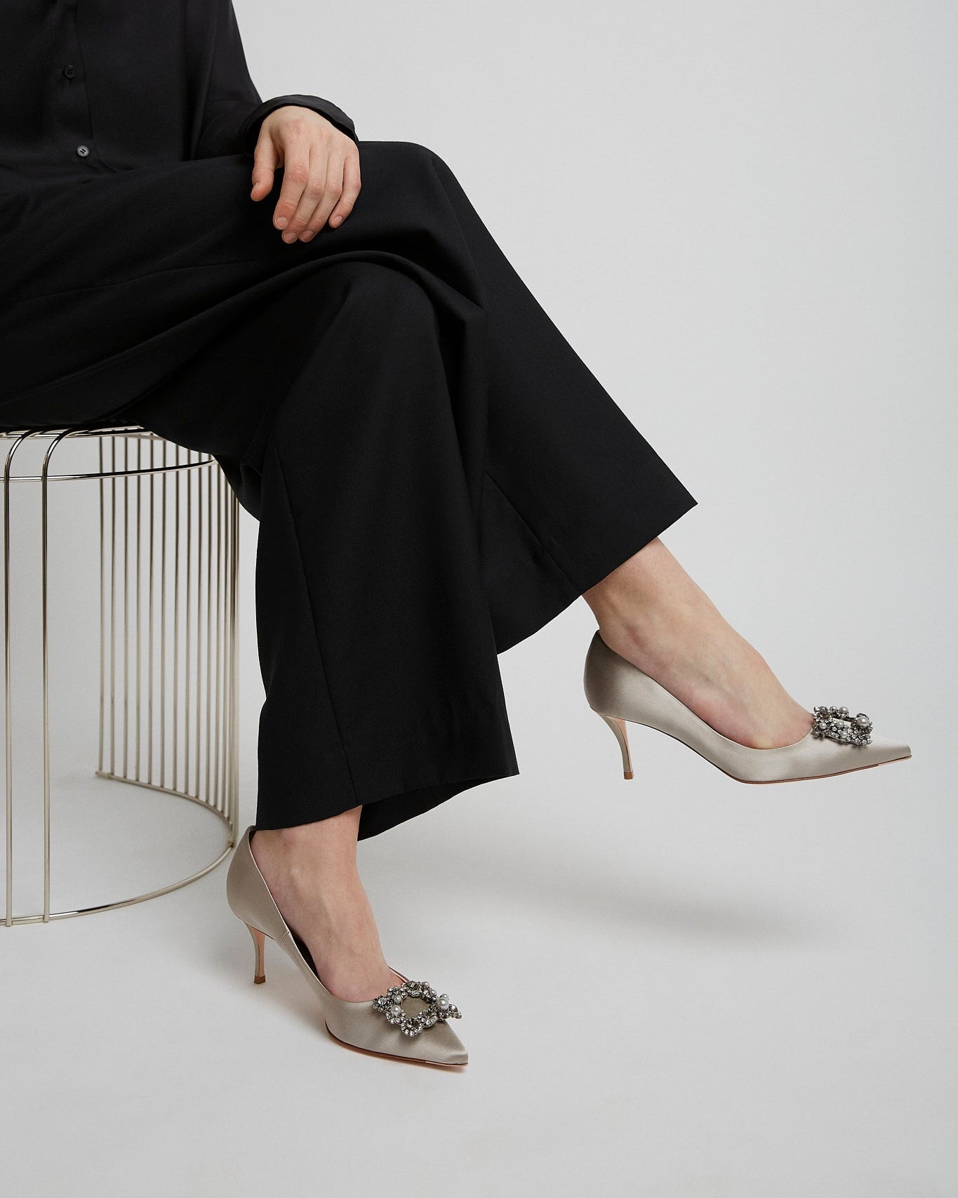 Person wearing black outfit and beige high-heeled shoes with decorative embellishments on a white background