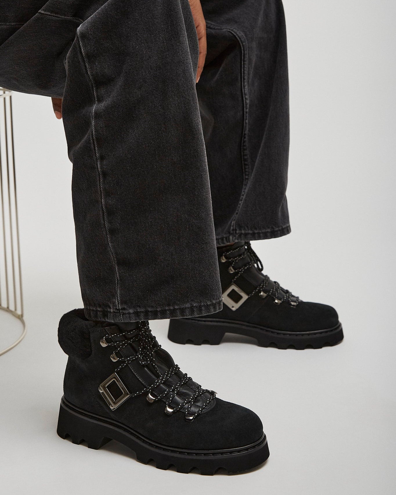 Person wearing black boots and dark jeans sitting on a white chair.
