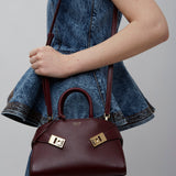 Person holding a maroon handbag with gold accents against a plain background