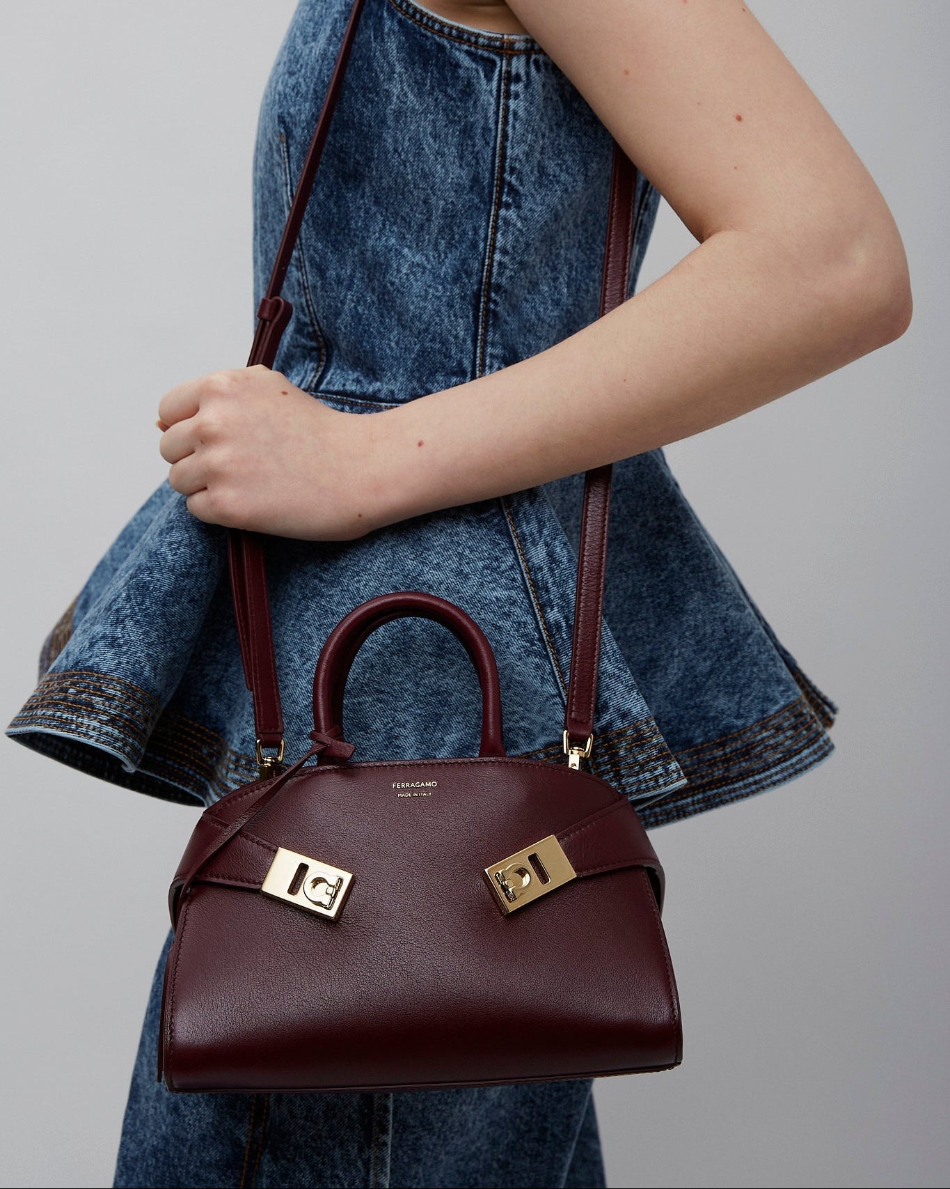 Person holding a maroon handbag with gold accents against a plain background