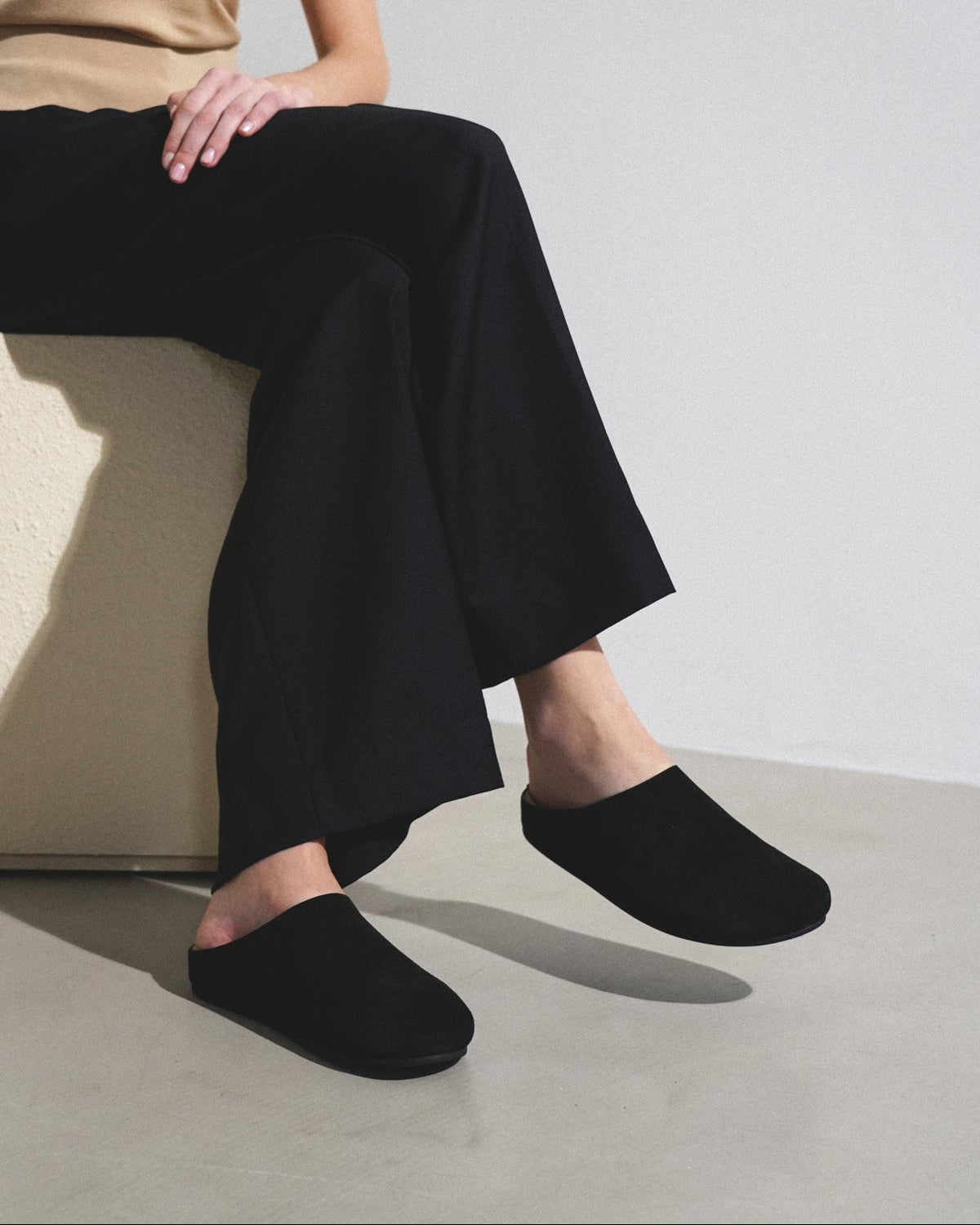 Person wearing black slippers and wide-leg pants sitting on a chair against a plain background