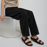 Person wearing a beige tank top and black pants sitting on a white stool against a plain background